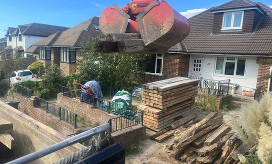 Excavator lifting timber during garden landscaping. Home garden renovation in progress.
